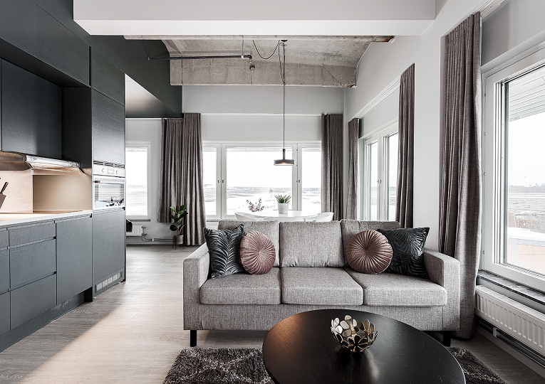 Hotellrum med skrivbord och grön stol, blå matta, två bäddar med rostfärgade filtar samt ljusinsläpp från stort fönster med orange gardiner.